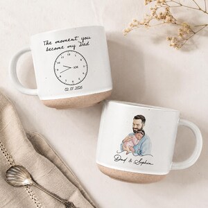 May include: Two white ceramic mugs with a beige base. One mug has the text "The moment you become my Dad" and a clock graphic. The other mug features a watercolor illustration of a father and child with the text "Dad & Sophia".