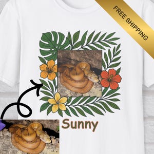 May include: White t-shirt with a graphic of an orange snake coiled inside a square frame of green leaves and orange and yellow flowers. The word "Sunny" is printed below the graphic. A gold banner in the upper right corner reads "FREE SHIPPING".