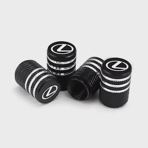 May include: Set of five black tire valve stem caps with silver accent rings and a white Lexus logo. The caps are cylindrical with a textured surface and are designed to protect the tire valves.