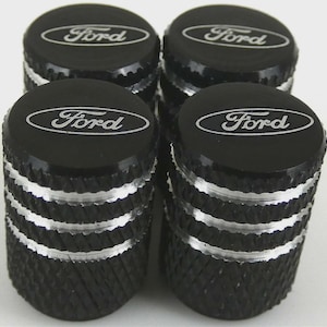 May include: Set of four black tire valve stem caps with the Ford logo in silver. The caps have a textured, diamond-patterned body with silver accent rings. The Ford logo is centered on the top of each cap.