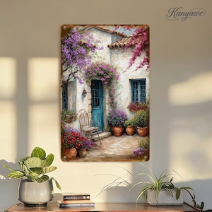 May include: Metal wall art featuring a picturesque scene of a white stucco building with a teal door and windows, adorned with vibrant purple flowers and potted plants. A small chair sits near the door. The artwork is signed "Kanyawe".