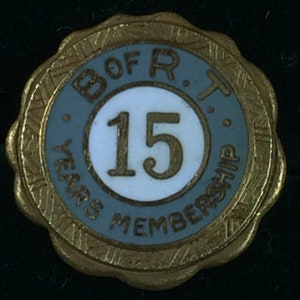 May include: A vintage gold-toned pin with a light blue and white center. The center features the number "15" in gold, surrounded by the words "YEARS MEMBERSHIP" and "B OF R T". The pin has a scalloped edge.