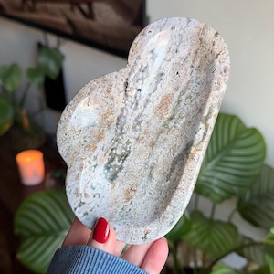 May include: A cloud-shaped stone tray featuring a polished surface with a mottled pattern in shades of beige, gray, white, and brown. The natural mineral texture displays intricate swirls and speckles throughout the entire curved form.