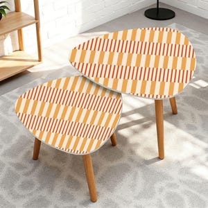 May include: A set of two nesting tables with irregular, rounded triangular tops. The surfaces feature a repeating geometric pattern of vertical stripes in alternating shades of light orange, cream, and dark brown. Each table has three light wood legs.