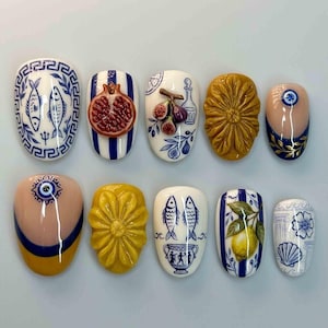 Peut inclure: Dix faux ongles décorés de motifs variés. Les motifs incluent des poissons, des grenades, des figues, des fleurs et un œil protecteur, dans des couleurs comme le bleu, le blanc, le jaune et le rouge. Les ongles sont de forme ovale.