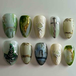 Könnte beinhalten: Ein Set aus zehn mandelförmigen Kunstnägeln mit verschiedenen Designs. Die Nägel weisen eine Reihe von Farben auf, darunter Grün, Gold und Weiß. Einige Nägel haben metallische Akzente, wie ein silbernes Blatt oder eine goldene Spirale. Andere Nägel haben Hirschgeweihe oder ein Schwertdesign.