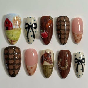 May include: A set of ten almond-shaped false nails with various designs. The designs include a red barn, a black bow, a carrot and apple, a brown checkered pattern, and a horse. The nails are painted in a variety of colors, including red, brown, white, and pink.