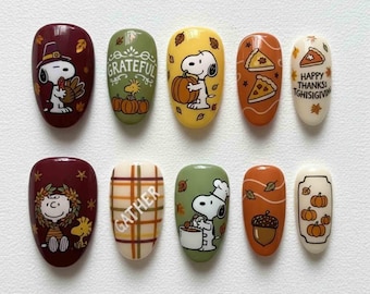 May include: A set of ten artificial nails with Thanksgiving-themed designs. The nails feature cartoon characters, pumpkins, pie slices, and the words "Grateful", "Gather", and "Happy Thanksgiving". Colors include burgundy, green, yellow, orange, and cream.