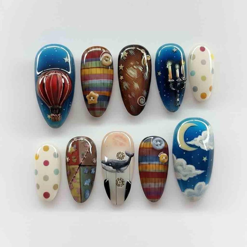 Puede incluir: Diez u&ntilde;as pintadas con diversos dise&ntilde;os. Los dise&ntilde;os incluyen un globo aerost&aacute;tico, patrones de rayas, estrellas, una ballena y una luna creciente con nubes. Las u&ntilde;as son ovaladas y tienen un acabado brillante.