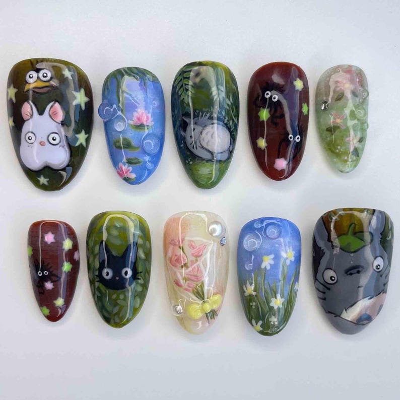 May include: A set of ten almond-shaped, painted fingernails. Each nail features a different design, including cartoon characters, flowers, and nature scenes. Colors include green, blue, red, and white. The designs are detailed and artistic, showcasing nail art.