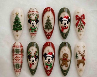 Puede incluir: Un juego de diez uñas postizas en forma de almendra con diseños navideños que incluyen a Mickey Mouse con ropa festiva, un hombre de jengibre, un reno, un lazo rojo y pinos verdes, decorados con detalles de estrellas doradas.