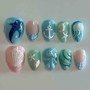Puede incluir: Un conjunto de diez u&ntilde;as artificiales con tem&aacute;tica de playa de verano. Los dise&ntilde;os incluyen un tibur&oacute;n ballena, ancla, concha, estrella de mar, medusa y patrones ondulados. Los colores incluyen azul, rosa y verde.