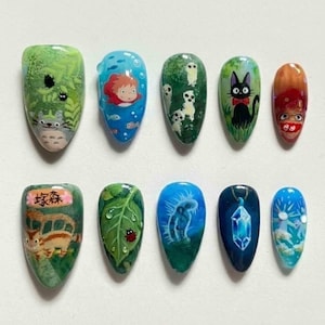 May include: A set of ten artificial nails, each uniquely designed with cartoon characters and nature scenes. The designs include a Totoro scene, a girl in the ocean, a black cat, and a leaf with a ladybug. The nails are painted in various colors.