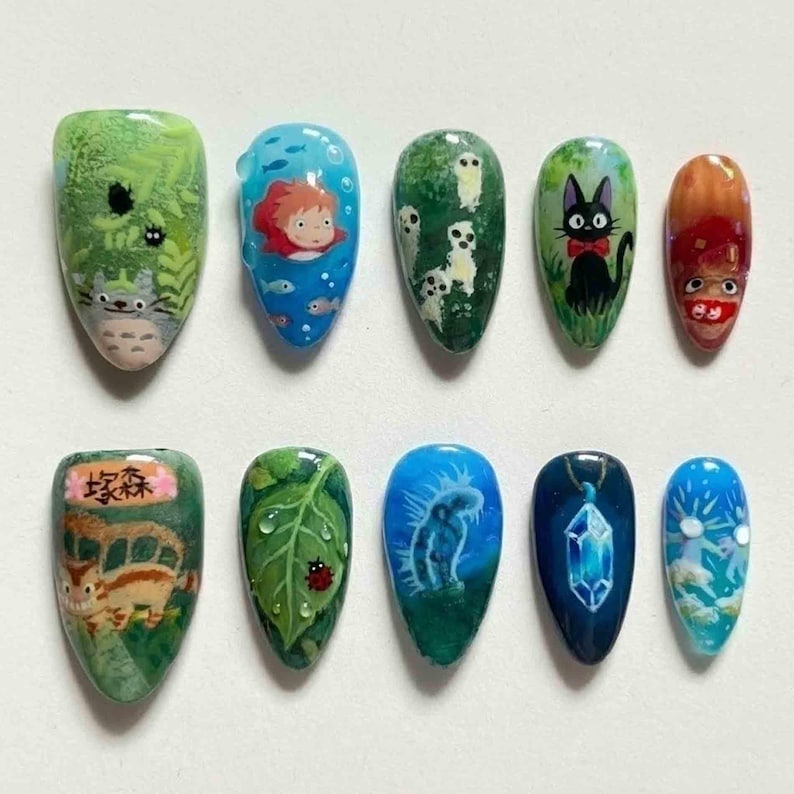 May include: A set of ten artificial nails, each uniquely designed with cartoon characters and nature scenes. The designs include a Totoro scene, a girl in the ocean, a black cat, and a leaf with a ladybug. The nails are painted in various colors.