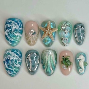 Könnte beinhalten: Ein Set aus zehn künstlichen Nägeln mit Meeresmotiven. Designs umfassen Ozeanwellen, einen Seestern, Muscheln, ein Seepferdchen und eine Meeresschildkröte. Die Nägel weisen Blau-, Grün- und Rosatöne mit Glitzer und 3D-Elementen auf.