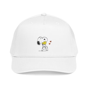 Op de afbeelding: Witte baseballpet met een Snoopy en Woodstock afbeelding. De stripfiguren zijn afgebeeld in zwart, geel en rood, met Snoopy die Woodstock kust. De pet heeft een gebogen klep en een klassiek zes-panelen ontwerp.