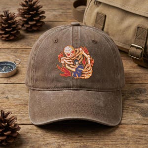 May include: Brown baseball cap with a distressed finish. The cap features a colorful graphic of a skeleton embracing a figure, surrounded by flames. The cap has a curved brim and an adjustable strap.