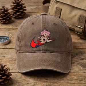May include: Brown baseball cap with a red and black graphic design. The design features a character with pink hair and a red swoosh. The cap is made of a soft material and has a curved brim.
