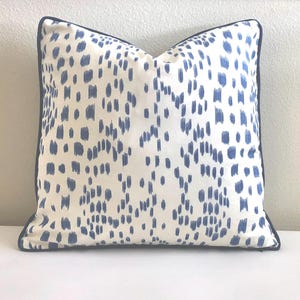 May include: Square decorative pillow with a white background and a pattern of blue brushstrokes. The pillow has a dark blue border. The pillow is a home decor item.