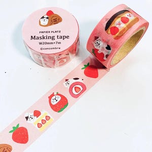 Puede incluir: Rollo de cinta adhesiva rosa con un patrón repetido de fresas, gatos y pasteles. La cinta adhesiva está etiquetada como "Masking tape" y mide 20 mm de ancho y 7 m de largo.