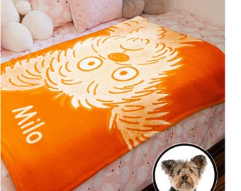 May include: Orange fleece blanket featuring a white cartoon dog face and the name "Milo" printed on it. A small dog is pictured in the bottom right corner.