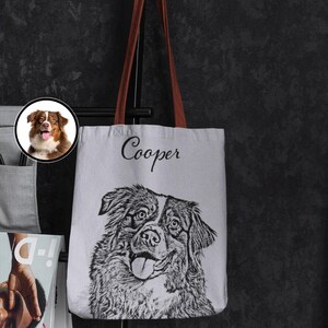 Puede incluir: Una bolsa de lona blanca con asas marrones. La bolsa presenta una ilustraci&oacute;n en blanco y negro de un perro con el nombre "Cooper" impreso en cursiva negra sobre el perro.
