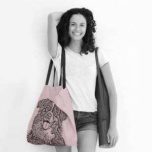 Puede incluir: Una mujer lleva una bolsa de tela rosa con una ilustraci&oacute;n en blanco y negro de un perro. Tambi&eacute;n lleva una esterilla de yoga negra.