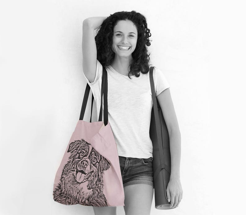 Puede incluir: Una mujer lleva una bolsa de tela rosa con una ilustraci&oacute;n en blanco y negro de un perro. Tambi&eacute;n lleva una esterilla de yoga negra.