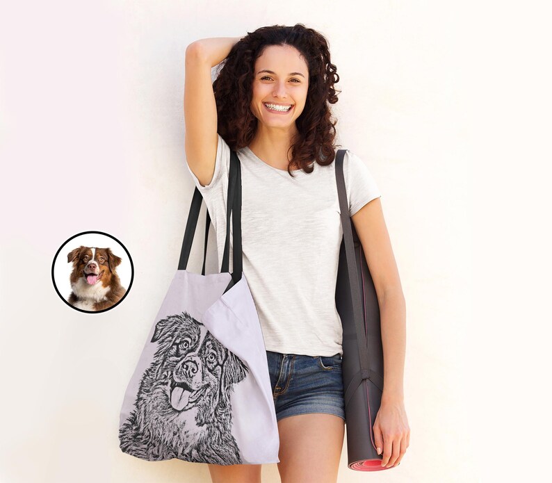 Puede incluir: Una mujer lleva una bolsa de tela negra y blanca con una ilustraci&oacute;n de un perro. La bolsa tiene correas negras y se lleva sobre el hombro de la mujer. Tambi&eacute;n lleva una esterilla de yoga enrollada.
