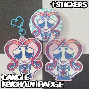 May include: A set of stickers, a keychain, and two badges featuring a cartoon character with a heart-shaped design. The character has blue eyes, a pink face, and a sailor uniform. The keychain has a blue heart-shaped clasp. The text "+STICKERS" and "GANGLE KEYCHAIN | BADGE" are visible.