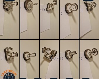 Puede incluir: Un conjunto de diez chinchetas magnéticas de madera cortadas con láser que presentan varios iconos como un copo de nieve, bastón de caramelo, carrito de compra, calendario, vaca y signo de interrogación para sujetar notas de papel.