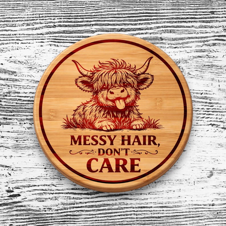 May include: A round bamboo cutting board featuring a laser-engraved illustration of a shaggy Highland cow with its tongue sticking out. The text "MESSY HAIR, DON'T CARE" is engraved below the cow, all enclosed within a circular border line.