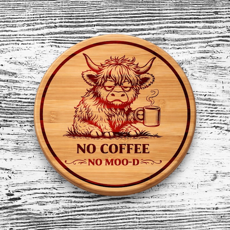 May include: A round bamboo coaster featuring a dark red engraved illustration of a shaggy Highland cow holding a coffee mug. The text NO COFFEE NO MOO-D is printed below the cow, all enclosed within a dark red circular border on the wood.