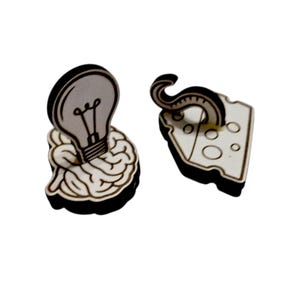 May include: Wooden earrings featuring a lightbulb over a brain and a tentacle over a cheese wedge. The earrings have a black outline and are made of light-colored wood. The lightbulb is gray with a black filament.