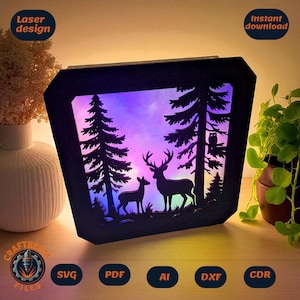 May include: A black laser-cut wooden light box featuring a silhouette of a deer and a fawn in a forest with pine trees and an owl. The background displays a vibrant purple and blue gradient light effect. Text includes Laser design and Instant download.