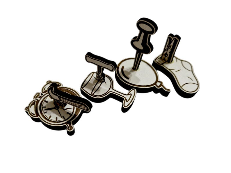 May include: Wooden cutouts of various objects, including an alarm clock with a bird, a wine glass with a corkscrew, a balloon with a push pin, and a sock with a clothespin. The objects are light brown with black accents.