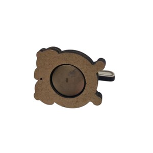 May include: A wooden magnet with a decorative bear shape. The bear is brown with a dark brown outline and a silver-colored metal loop. A circular magnet is visible on the back.
