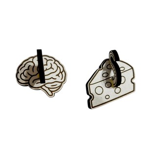 May include: Two wooden earrings: one shaped like a brain and the other like a slice of cheese. Both earrings have a black post and are light brown with black outlines. The brain earring has a vertical black line through it.