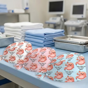 May include: Three surgical scrub caps with a repeating cartoon stomach design in white, pink, and light blue. Each cap has the text "THEY HATE US CUZ THEY ANUS". The caps are on a light blue surface.