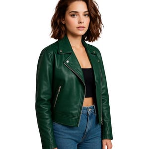 Könnte beinhalten: Dunkelgrüne Lederjacke im Biker-Stil. Sie hat einen Reverskragen, einen asymmetrischen Reißverschluss und silberfarbene Metallbeschläge. Das Model trägt ein schwarzes Top und blaue Jeans.