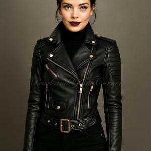 May include: A black leather motorcycle jacket featuring gold-tone zips, a notched collar with snap buttons, quilted shoulder panels, and a buckled waist belt. The jacket is worn over a black turtleneck jumper and paired with black leather gloves.