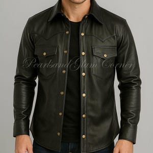 May include: Black leather shirt with a classic collar, two chest pockets, and gold-coloured buttons. The shirt has long sleeves and a tailored fit. The text "Pearlsand Glam Corner" is visible on the shirt.