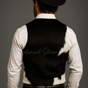 May include: A black and white cowhide vest worn over a crisp white long-sleeved button-down shirt, paired with black trousers and a black cowboy hat. The vest features a distinct spotted pattern with a solid black back panel and white accents.
