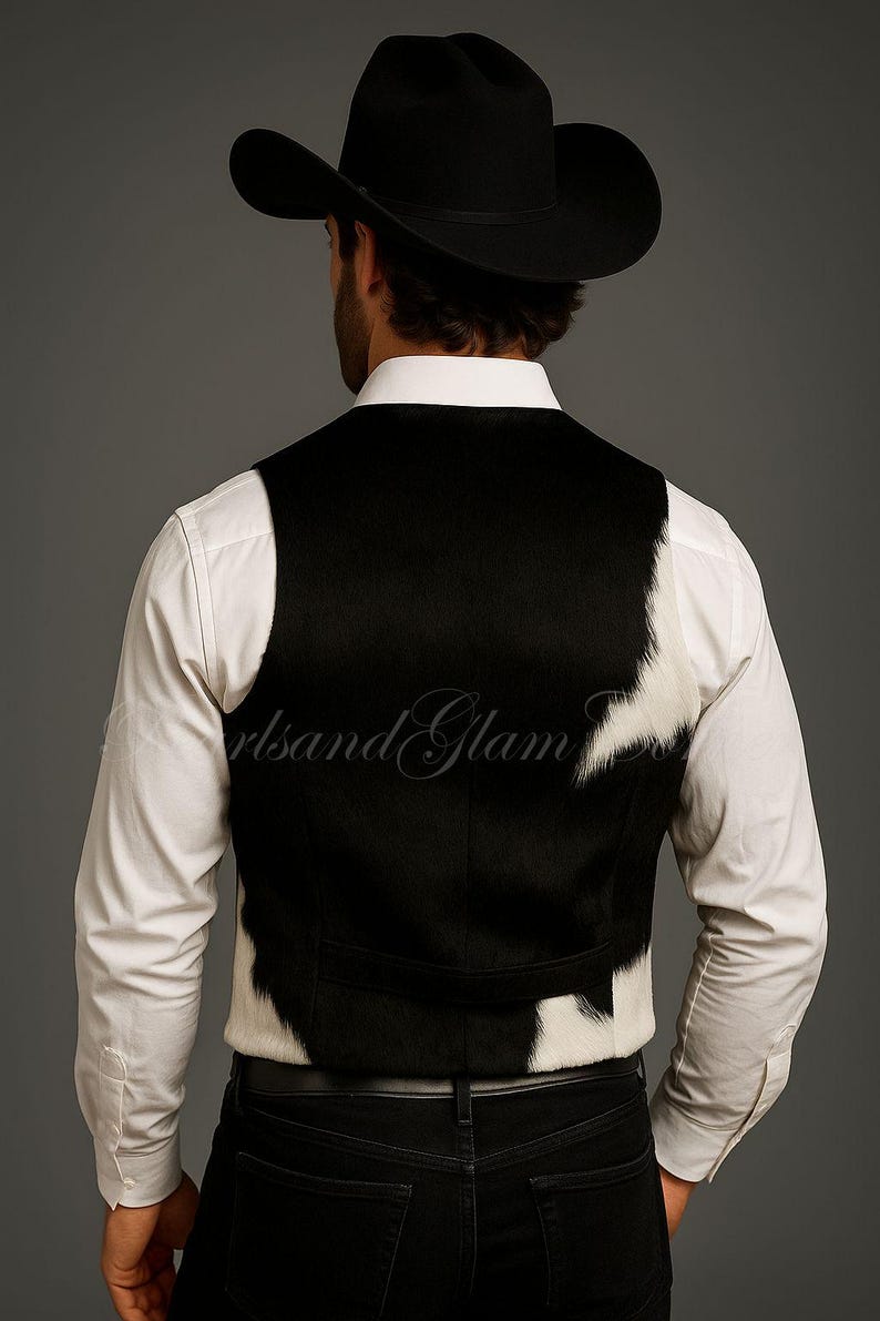 May include: A black and white cowhide vest worn over a crisp white long-sleeved button-down shirt, paired with black trousers and a black cowboy hat. The vest features a distinct spotted pattern with a solid black back panel and white accents.