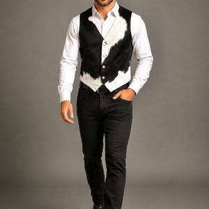 May include: A black and white cowhide print vest with silver buttons, worn over a crisp white long-sleeved button-down shirt, paired with black denim jeans, black leather boots, and a wide-brimmed black felt cowboy hat with a matching band.