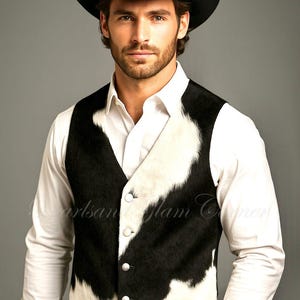 May include: A black and white cowhide vest featuring a V-neckline, four silver-toned buttons, and a textured hair-on-hide finish. The vest is worn over a crisp white long-sleeved button-down shirt, paired with a black cowboy hat.