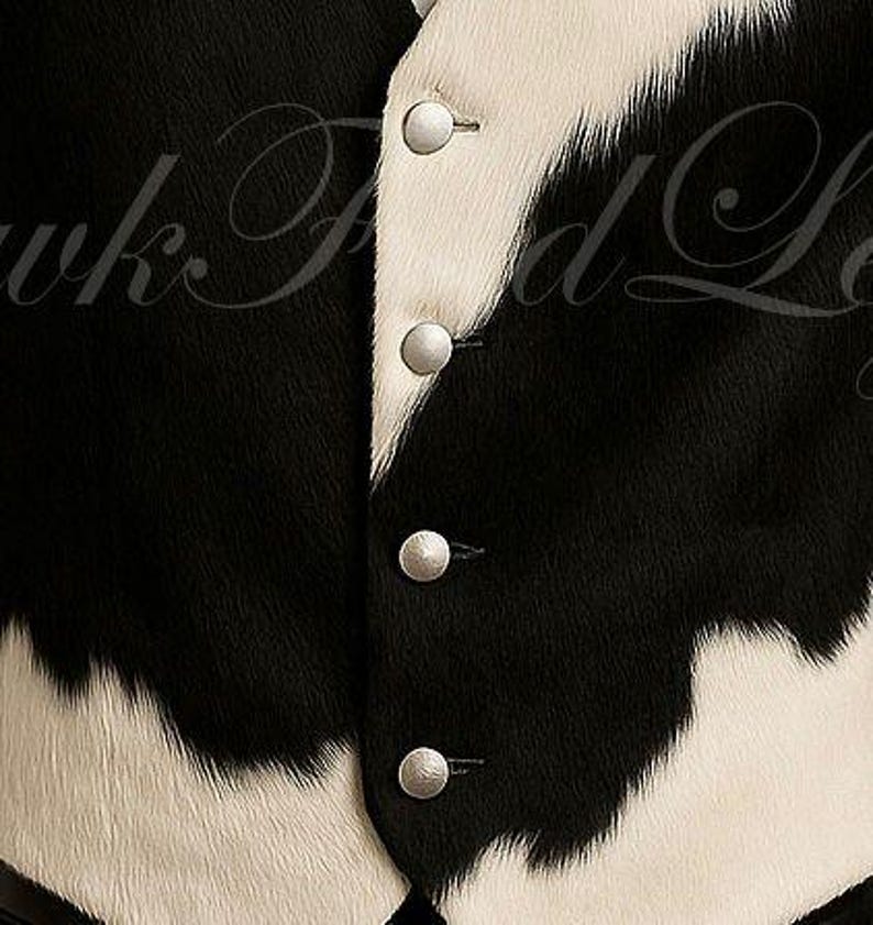 May include: A vest featuring a black and white cowhide pattern with a textured, fur-like appearance. The garment includes a front button closure with four round, silver-toned metallic buttons aligned vertically along the center placket.