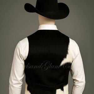 May include: A black cowboy hat worn with a white long-sleeved button-down shirt and a vest featuring a black and white cowhide pattern. The vest has a solid black back panel and a horizontal strap across the lower back area, worn over dark trousers.