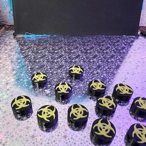May include: A collection of black cylindrical objects with a yellow biohazard symbol on top. The objects are arranged on a reflective, star-patterned surface. The background is a dark, solid color.