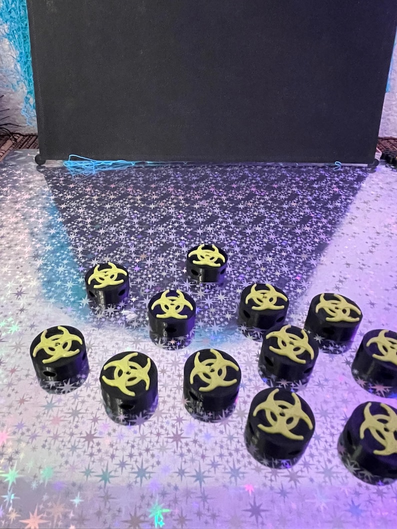 May include: A collection of black cylindrical objects with a yellow biohazard symbol on top. The objects are arranged on a reflective, star-patterned surface. The background is a dark, solid color.